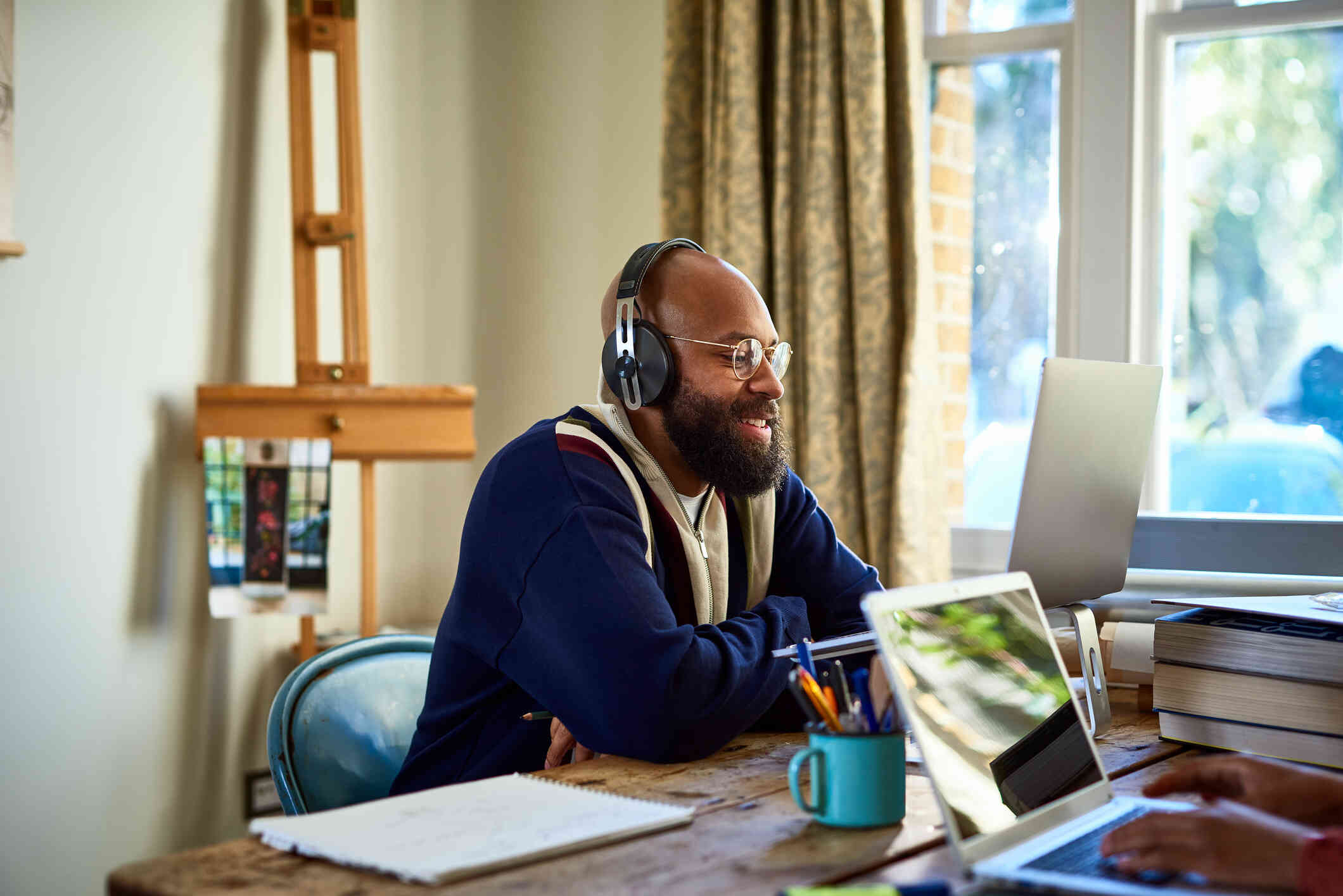 A man with his headphones on, smiles at his laptop screen.